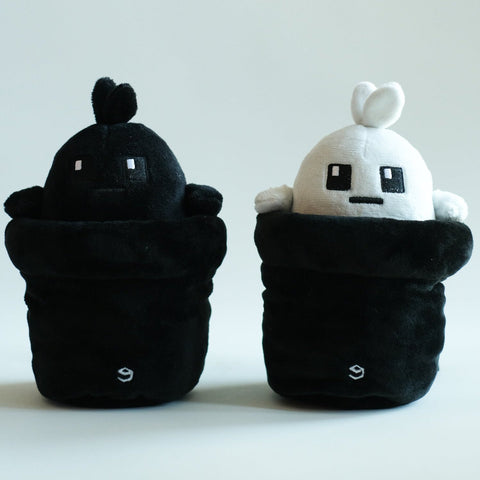 Two Potatoz plush toys, one black and one white, sitting on a light gray background.
