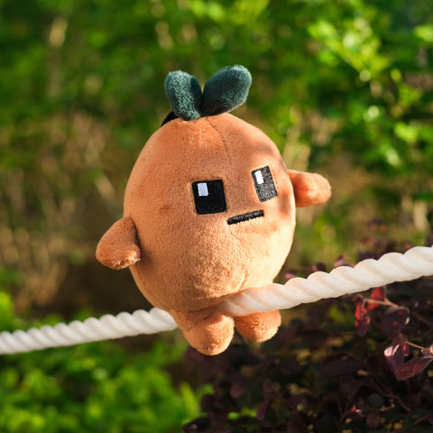 Potatoz plush toy resembling a character with a sad expression, hanging on a rope with a green leafy background.